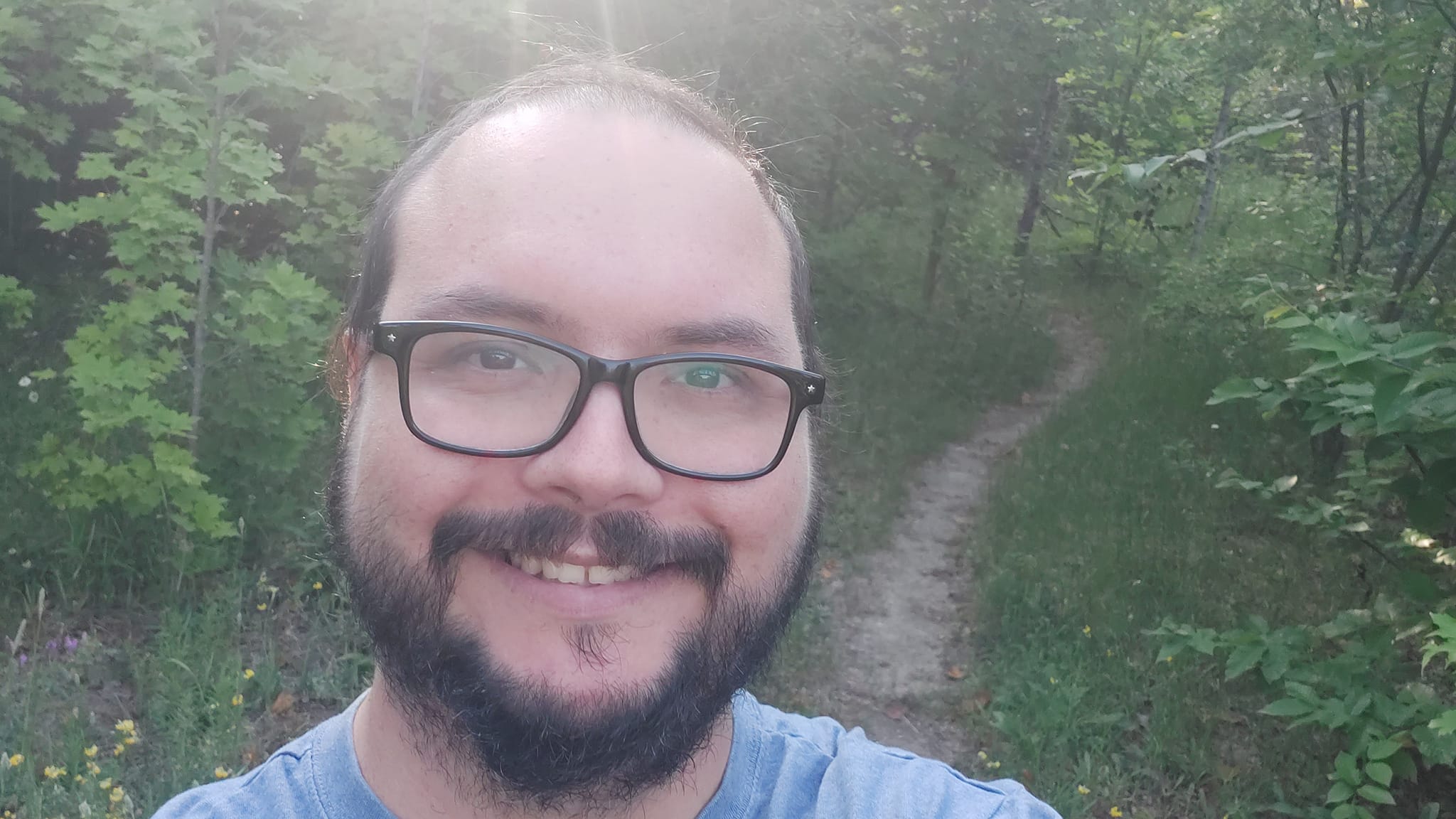 A man is dressed in a t-shirt standing in front of a path through the brush